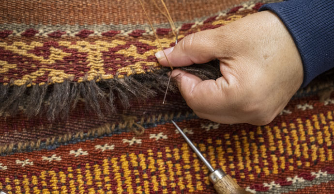 A technician performing detailed hand-sewing for rug fringe repair