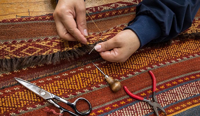 Close-up of rug fringe repair with scissors pliers and hand tools on a patterned rug