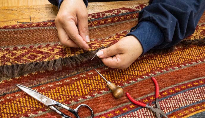 Technician sewing and repairing oriental rug fringe