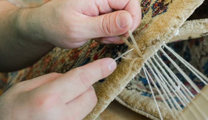 Technician sewing replacement yarn into oriental rug edge