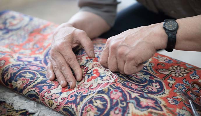 Technician stitching foundation backing threads on oriental rug