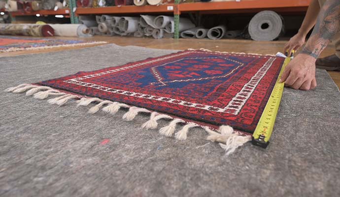 Worker measuring patterned rug dimensions with measuring tape