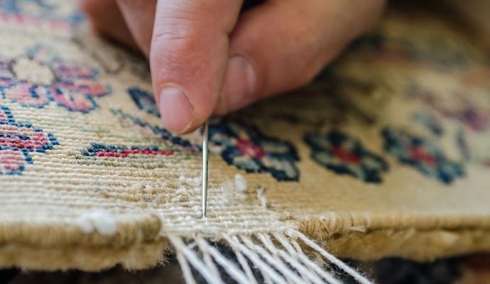 A person repairing rug using a needle