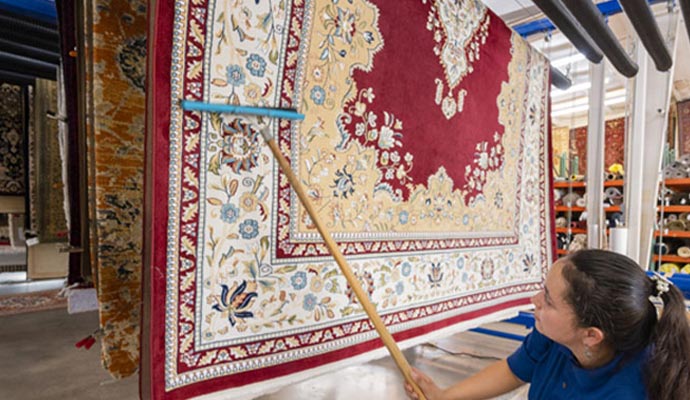 Professional rug washing process with a large hanging rug being cleaned in a facility